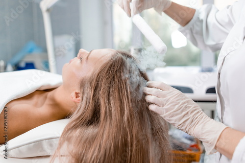 Beautiful girl at the reception of a dermatologist in the health clinic. Dermatologist conducting hair restoration procedure with liquid nitrogen