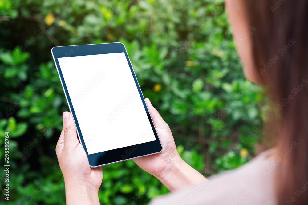 Mockup image of a woman holding black tablet pc with blank white desktop screen in the park