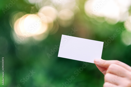 A hand holding a white blank business card with green nature background