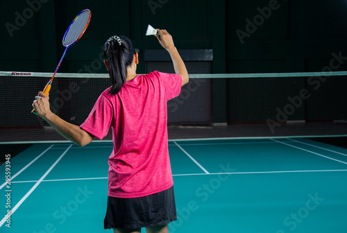 Back view Asian woman Badminton player in red sport shirt holding racket and shuttlecock ready to serve in green Badminton court. © Jack Tamrong