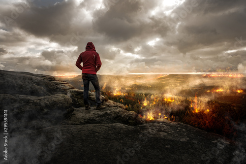 Mann steht auf einen Berg und schaut auf eine brennende Landschaft