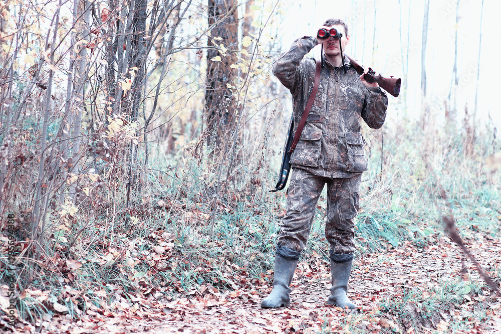 A man in camouflage and with a hunting rifle in a forest on a spring hunt
