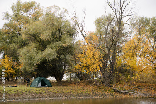 Camping green tent in forest near lake in autumn