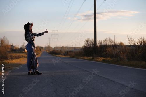 A young girl is traveling around the city hitchhiking. A beautiful young girl went on vacation. A female student in a cowboy hat on the road in autumn.