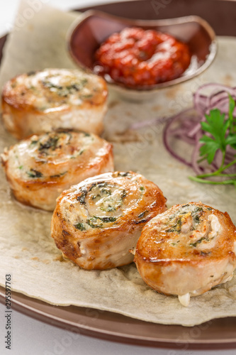 chicken breast roll stuffed with cheese and herbs and tomato sauce on brown plate
