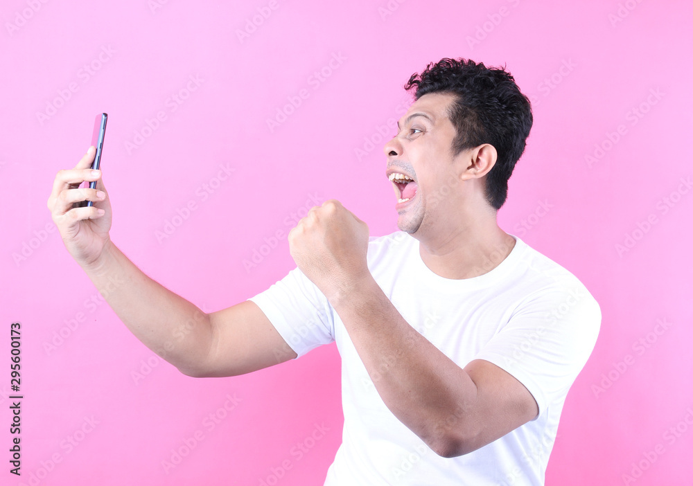 Wow face of Asian man shocked what he see in the smartphone isolated on a pink background in studio. Wow face of Asian man shocked what he see in the smartphone isolated on a pink background in studio.