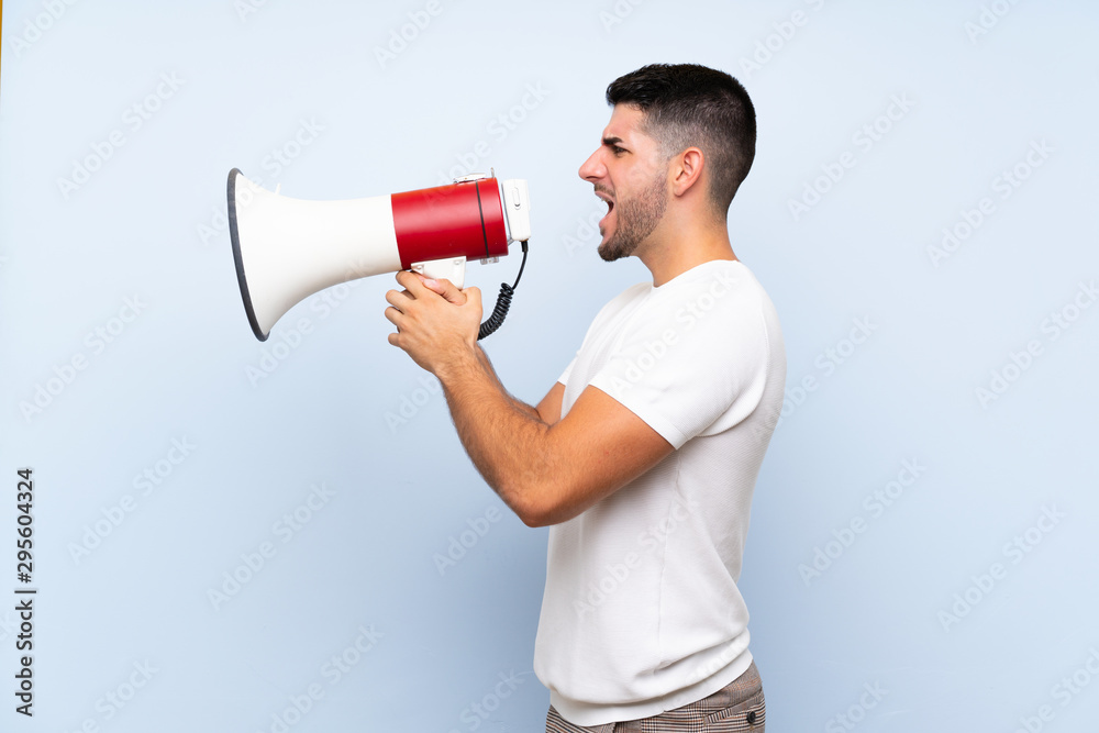 Caucasian handsome man over isolated blue background shouting through a megaphone Caucasian handsome man over isolated blue background shouting through a megaphone