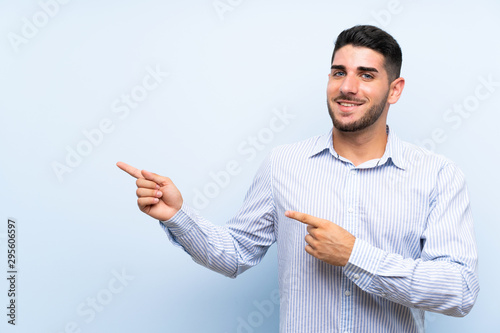 Caucasian handsome man over isolated blue background pointing finger to the side
