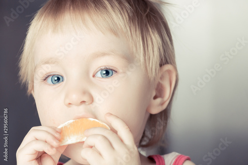 Beautiful child with large blue eyes tries orange slice.