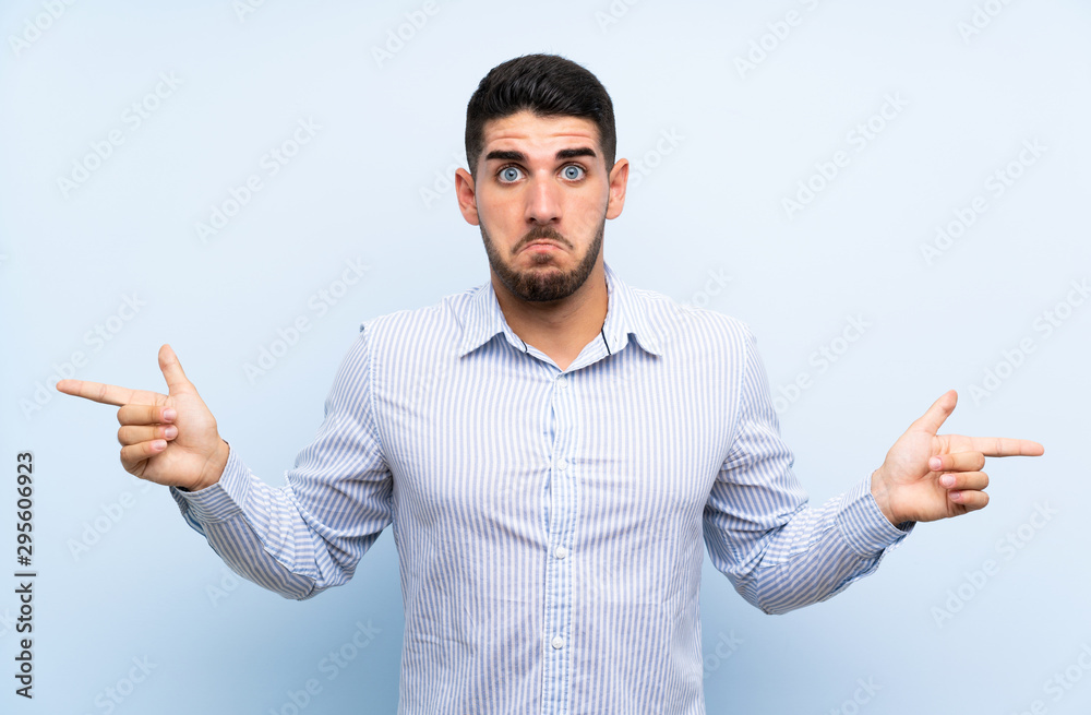 Caucasian handsome man over isolated blue background pointing to the laterals having doubts Caucasian handsome man over isolated blue background pointing to the laterals having doubts