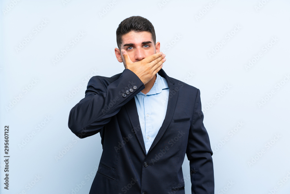 Handsome man over isolated blue background covering mouth with hands Handsome man over isolated blue background covering mouth with hands