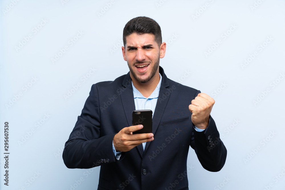 Handsome man over isolated blue background with phone in victory position Handsome man over isolated blue background with phone in victory position