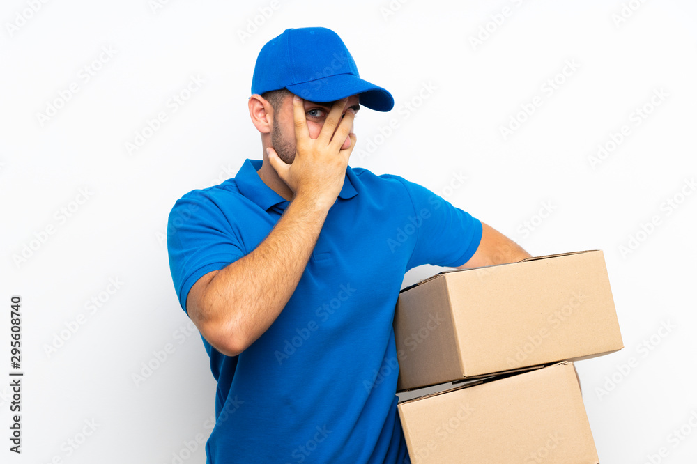 Delivery man over isolated white background covering eyes and looking through fingers Delivery man over isolated white background covering eyes and looking through fingers