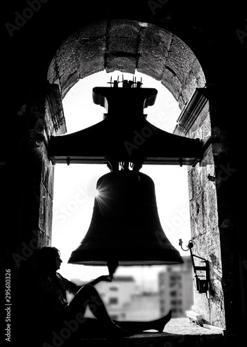 Silueta de mujer y campana en el campanario de iglesia con sol a contraluz