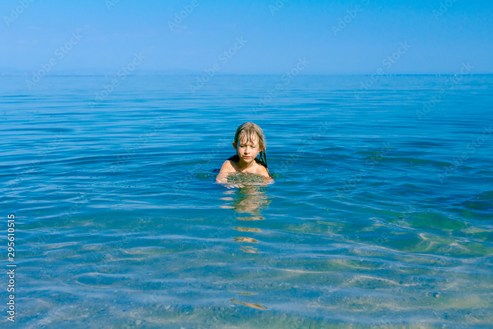 Excited child girl jumping with widespread hands in shallow sea water