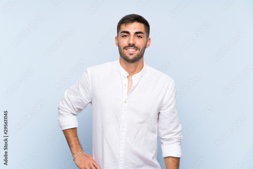 Handsome man with beard over isolated blue background posing with arms at hip and smiling Handsome man with beard over isolated blue background posing with arms at hip and smiling