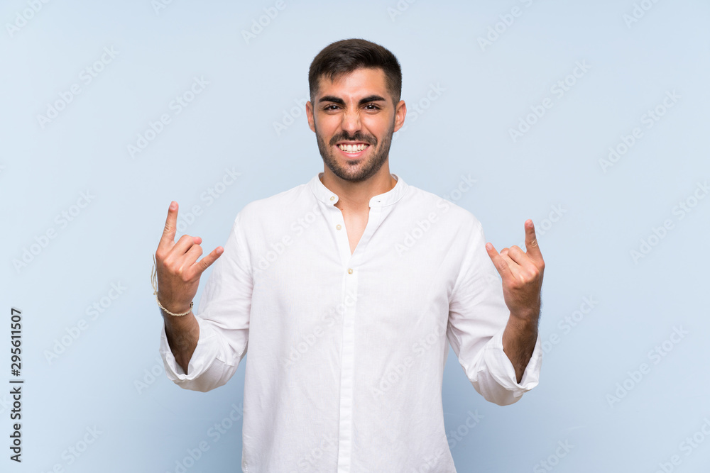 Handsome man with beard over isolated blue background making rock gesture Handsome man with beard over isolated blue background making rock gesture