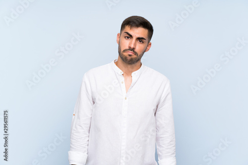 Handsome man with beard over isolated blue background with sad and depressed expression © luismolinero