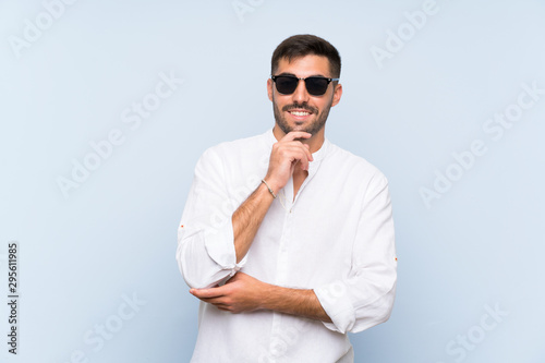 Handsome man with beard over isolated blue background with glasses and smiling