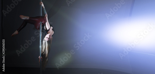 The dancer on the pylon in the studio. Girl doing exercises on a sports equipment.