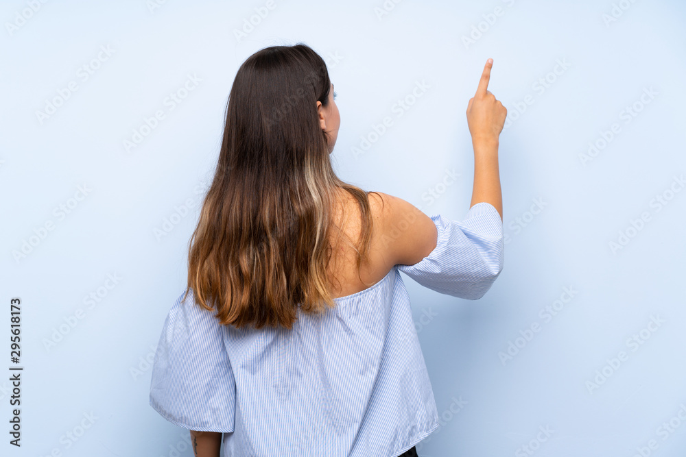 Young brunette woman over isolated blue background pointing back with the index finger Young brunette woman over isolated blue background pointing back with the index finger
