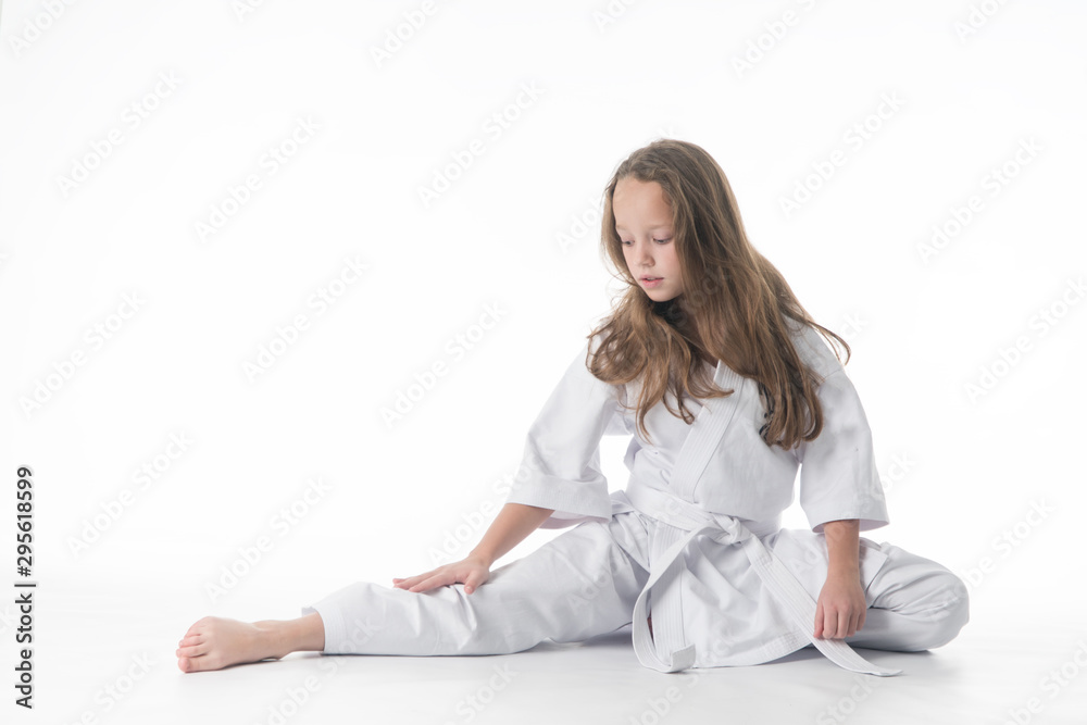 little karate girl in a white kimono and a  belt sits for a workout in sports twine