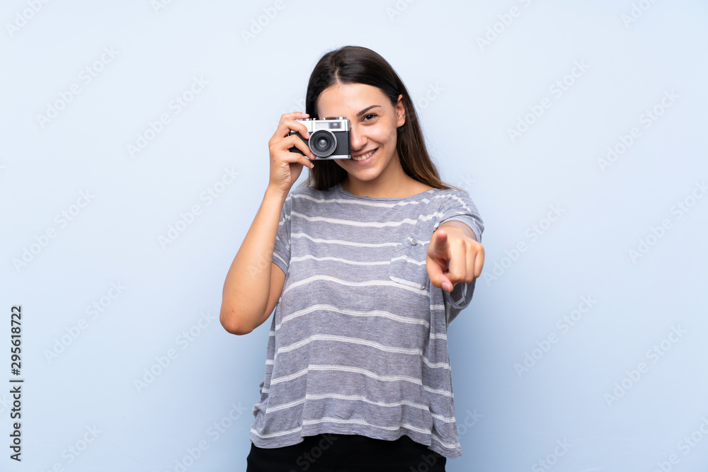 Young brunette woman over isolated blue background holding a camera Young brunette woman over isolated blue background holding a camera