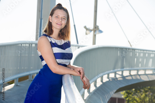 Girl in blue dress standing on city bridge