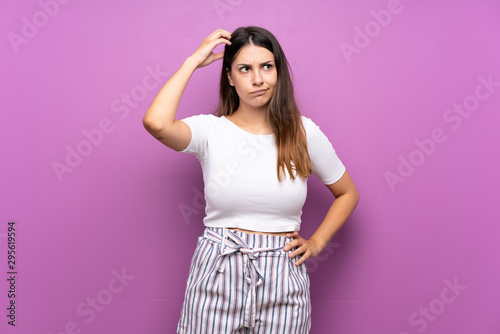 Young woman over isolated purple background having doubts while scratching head