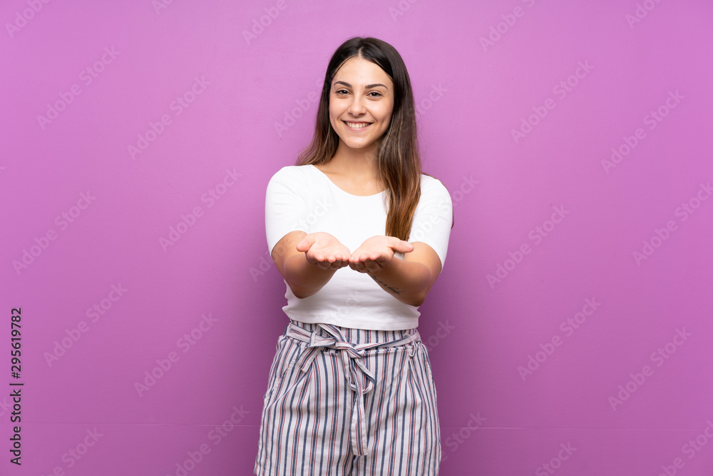 Young woman over isolated purple background holding copyspace imaginary on the palm to insert an ad Young woman over isolated purple background holding copyspace imaginary on the palm to insert an ad
