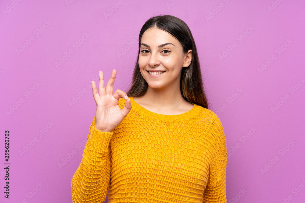 Young woman over isolated purple background showing an ok sign with fingers Young woman over isolated purple background showing an ok sign with fingers