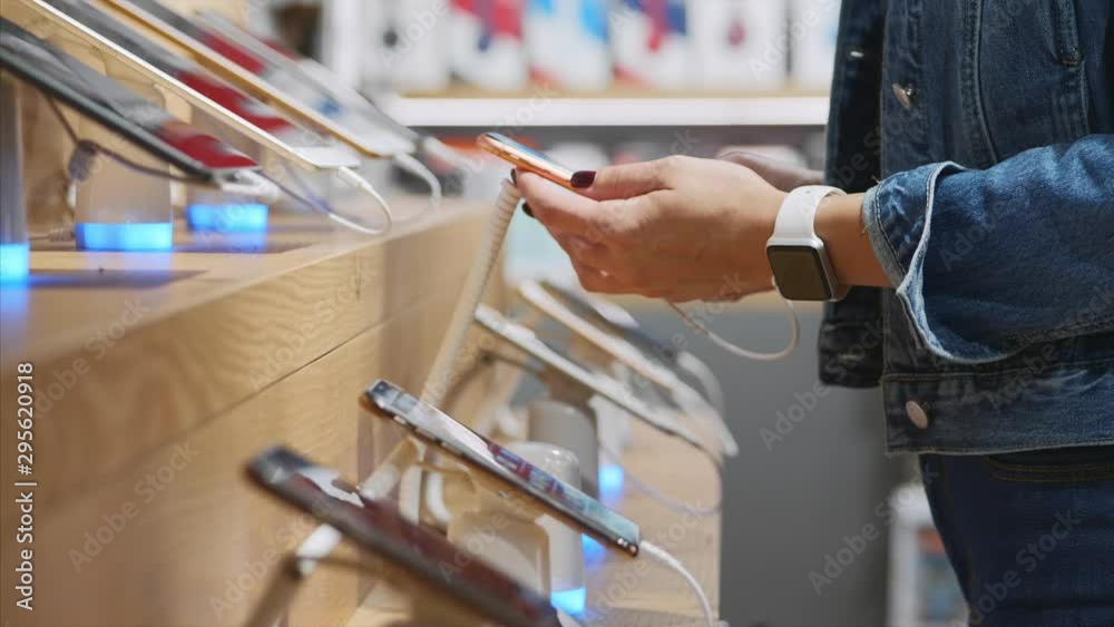 Young unrecognizable woman chooses a smartphone in an electronics store, close-up. She takes smart phone from counter and trying using it.