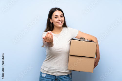Young delivery woman over blue brick wall inviting to come with hand. Happy that you came
