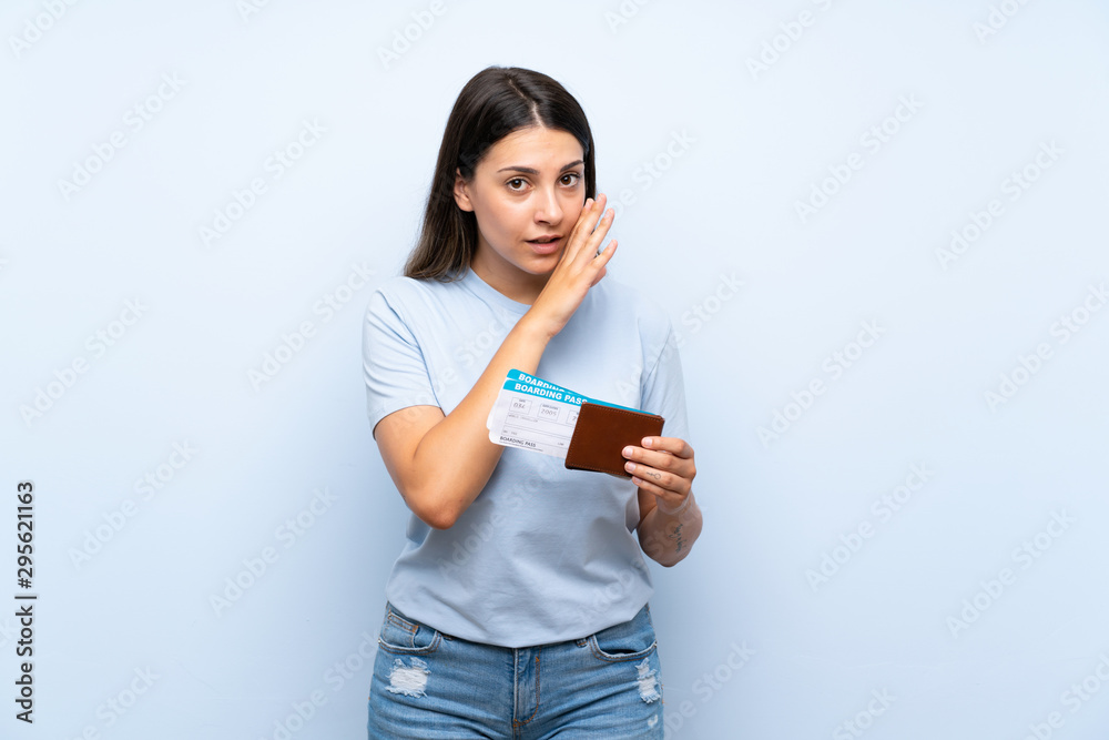 Traveler woman with boarding pass over isolated blue wall whispering something Traveler woman with boarding pass over isolated blue wall whispering something