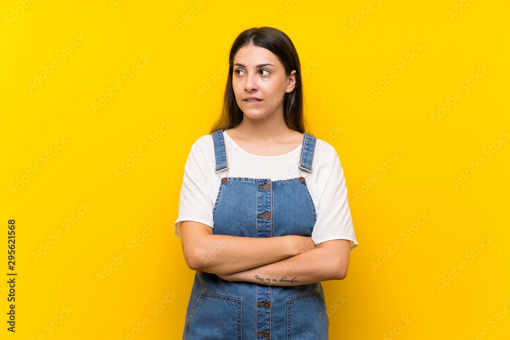 Young woman in dungarees over isolated yellow background with confuse face expression Young woman in dungarees over isolated yellow background with confuse face expression