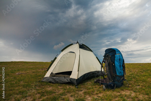 Empty tent with backpack of travelers on green terrain in bright sunset light