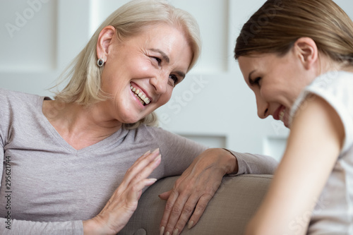 Cheerful older mother laughing talking with grown up daughter indoors