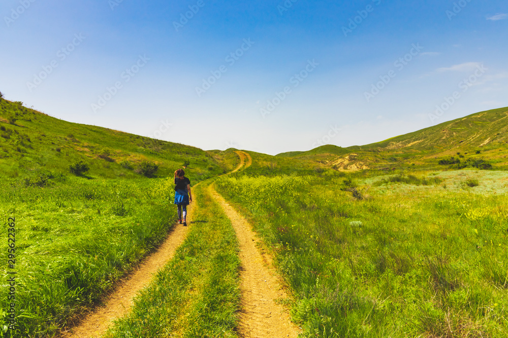 Large green field with a road in the center and a girl on it. Beautiful view of the field with a blue sky. Large green field with a road in the center and a girl on it. Beautiful view of the field with a blue sky.