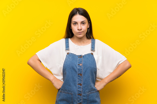 Young woman in dungarees over isolated yellow background angry