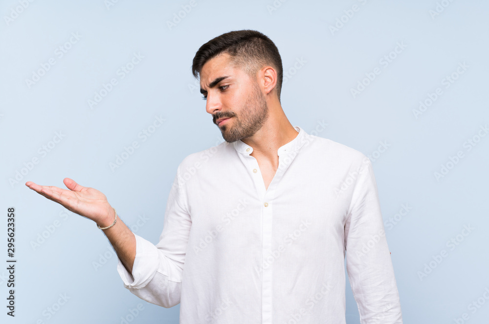Handsome man with beard over isolated blue background holding copyspace with doubts