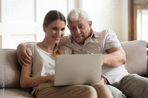 Grandfather and adult granddaughter sitting on couch using laptop
