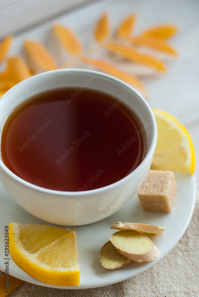 white cup of tea with lemon, ginger and brown sugar on the wooden table with autumn leaves white cup of tea with lemon, ginger and brown sugar on the wooden table with autumn leaves