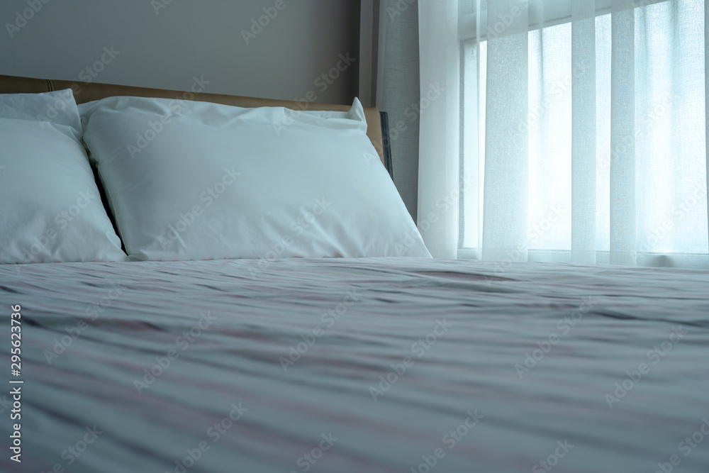 The white pillows on the soft bed with sheets with morning light outside the window.