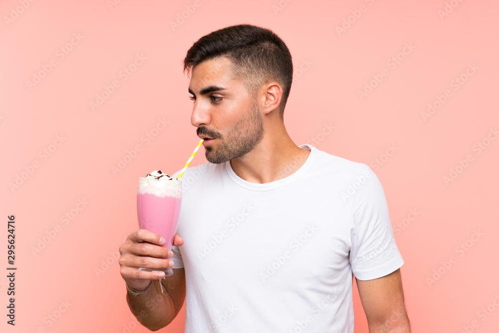 Young man with strawberry milkshake over isolated pink background Young man with strawberry milkshake over isolated pink background