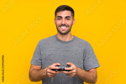 Young handsome man playing with a video game controller over isolated yellow background
