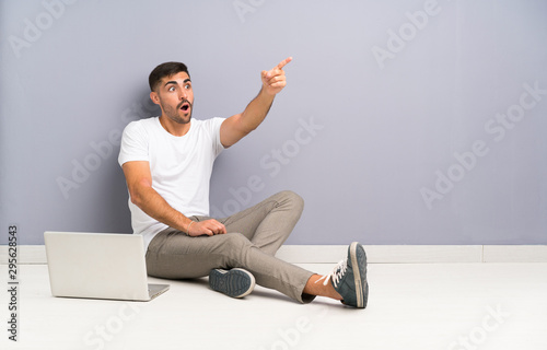 Young man with his laptop sitting one the floor pointing away