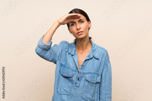 Young woman over isolated background looking far away with hand to look something