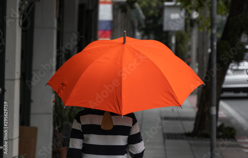 Back view of woman with orange umbrella walking on a street. © Volodymyr