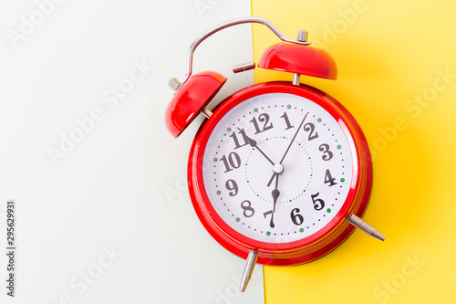 Red vintage alarm clock on yellow and white background