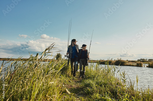 Caucasian father and son walk on islet among lake. They choose good place for fishing together to get big catch and then cook on fire